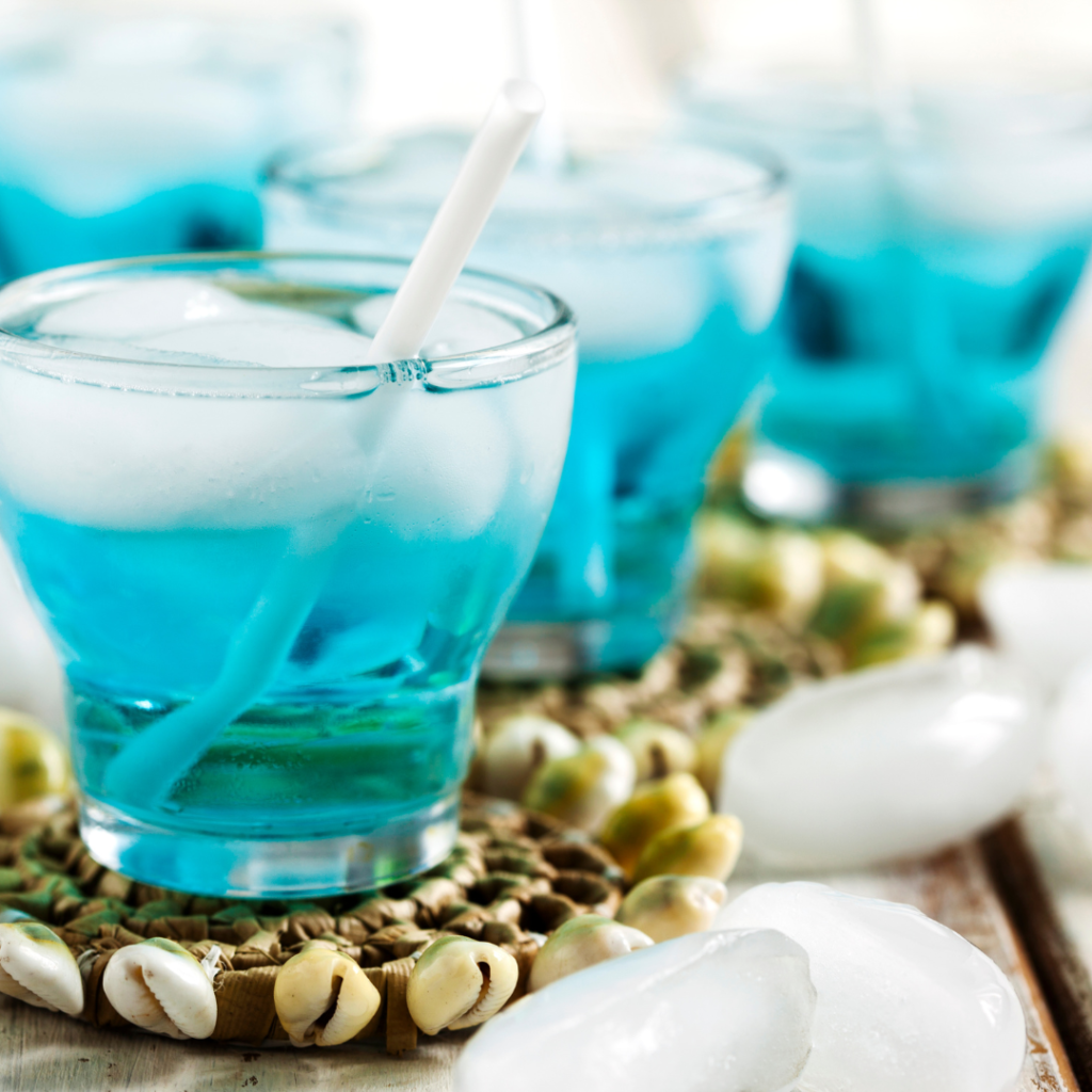 Blue cocktail resting on a coaster decorated with cowrie shells