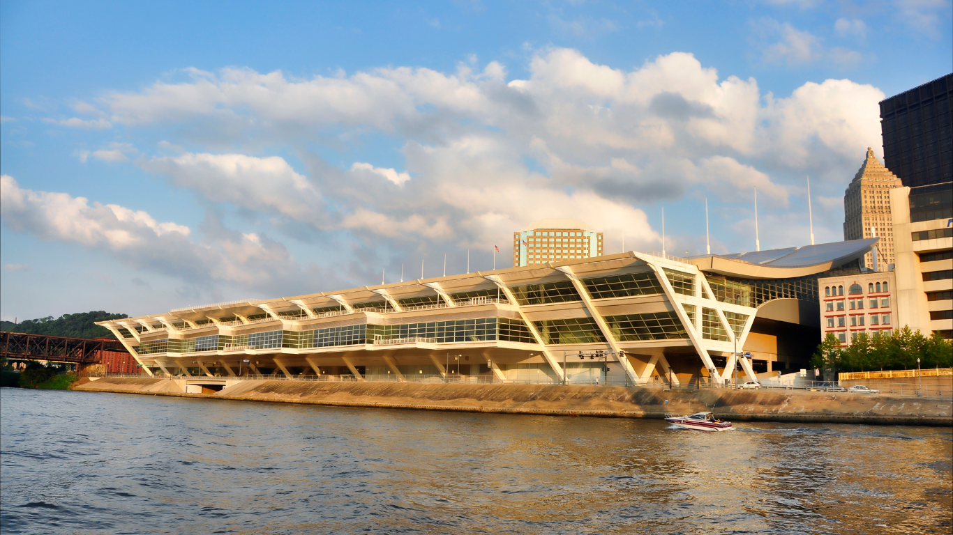 A riverside view of the David L. Lawrence Convention Center in Pittsburgh, featuring its modern architectural design with large glass windows and angular beams, illuminated by the golden evening light