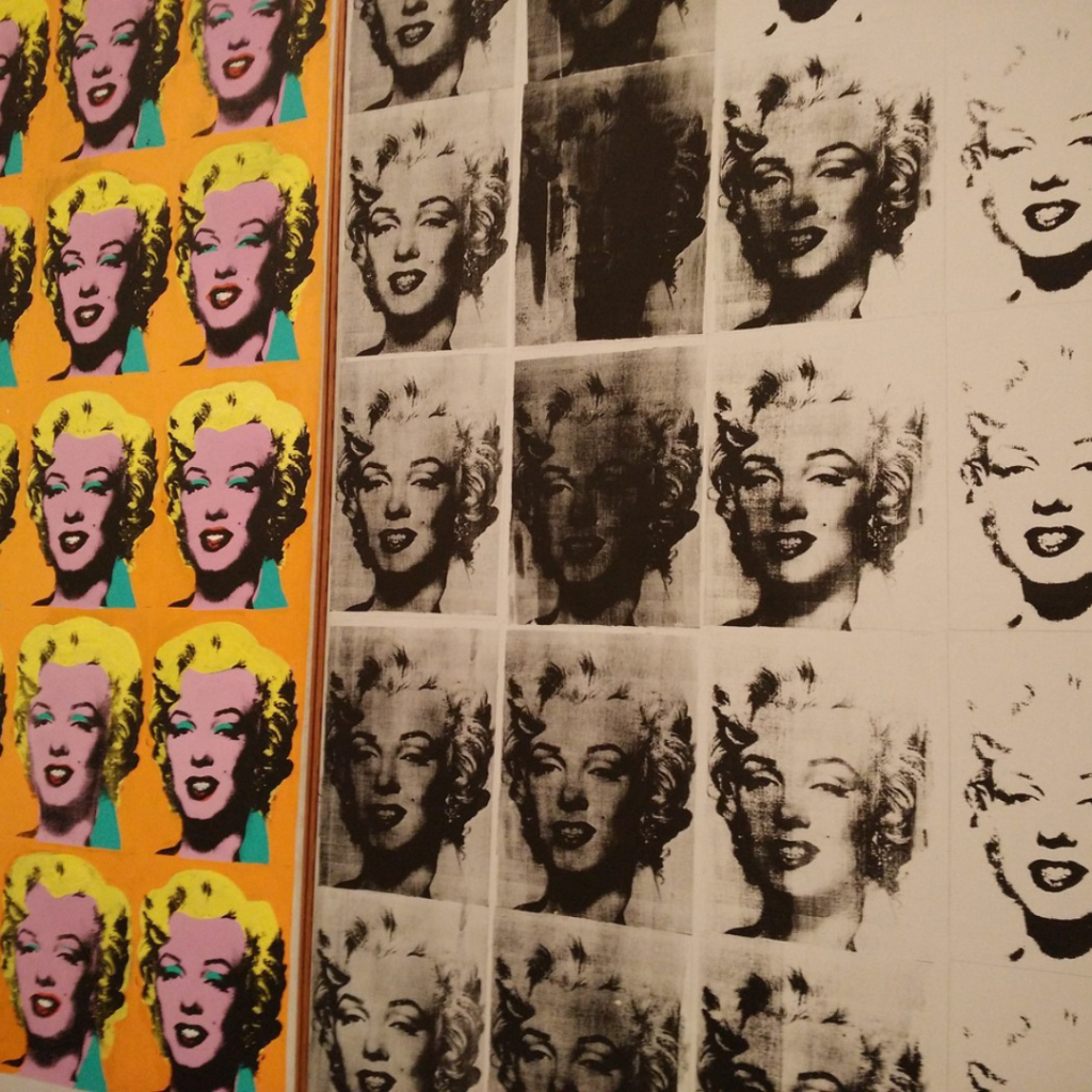 A display of Andy Warhol's famous Marilyn Monroe silkscreens, with vibrant, colorful portraits on the left and black-and-white variations on the right, showcasing Warhol's signature pop art style and exploration of celebrity culture.