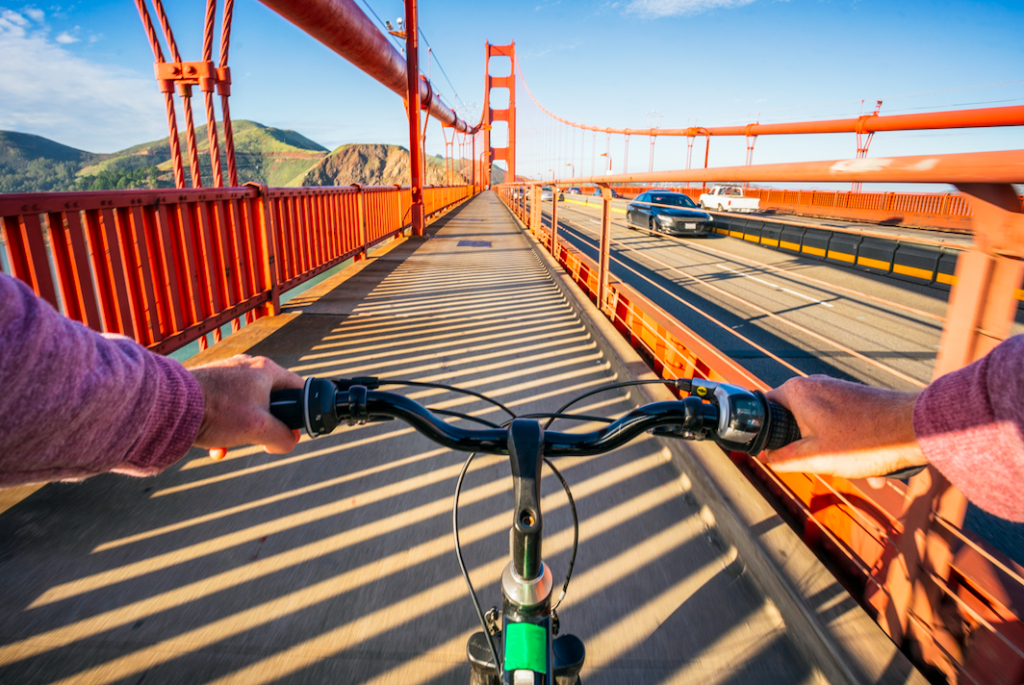 two hands on bike handlebars with the golden gate bridge in the background
