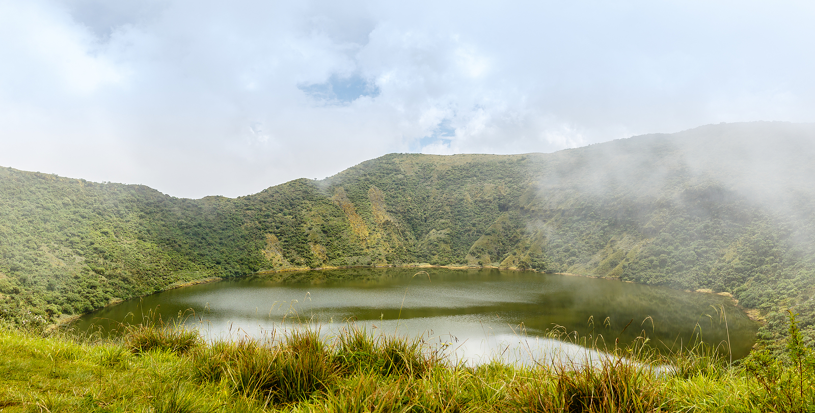 Scenic view of the crater lake inside Mount Bisoke volcano at Virunga National Park, Rwanda, surrounded by lush vegetation—popular destination for hiking and eco-tourism in East Africa.