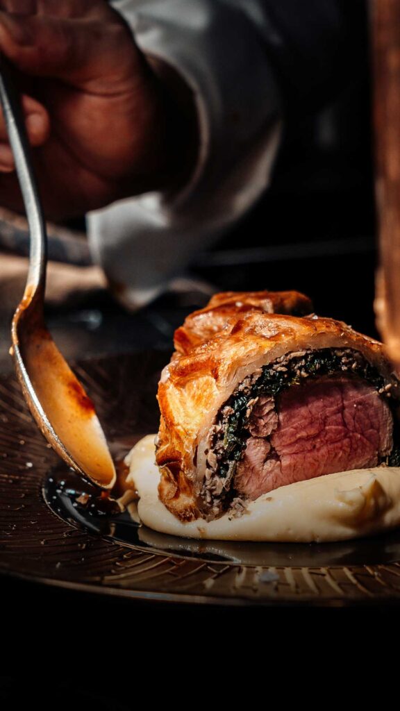 A gourmet beef Wellington dish topped with sauce and served on a bed of mashed potatoes