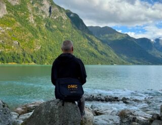 Man sitting on a boulder looking at the mountains in the distance across the water