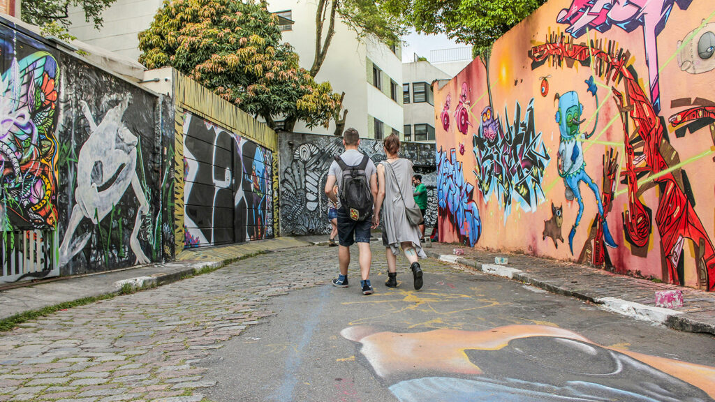 Two people walking down a street flanked with graffiti covered walls.