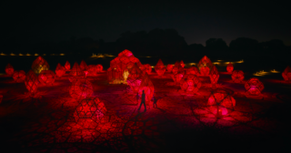 people standing in front of a red light sculpture display at night