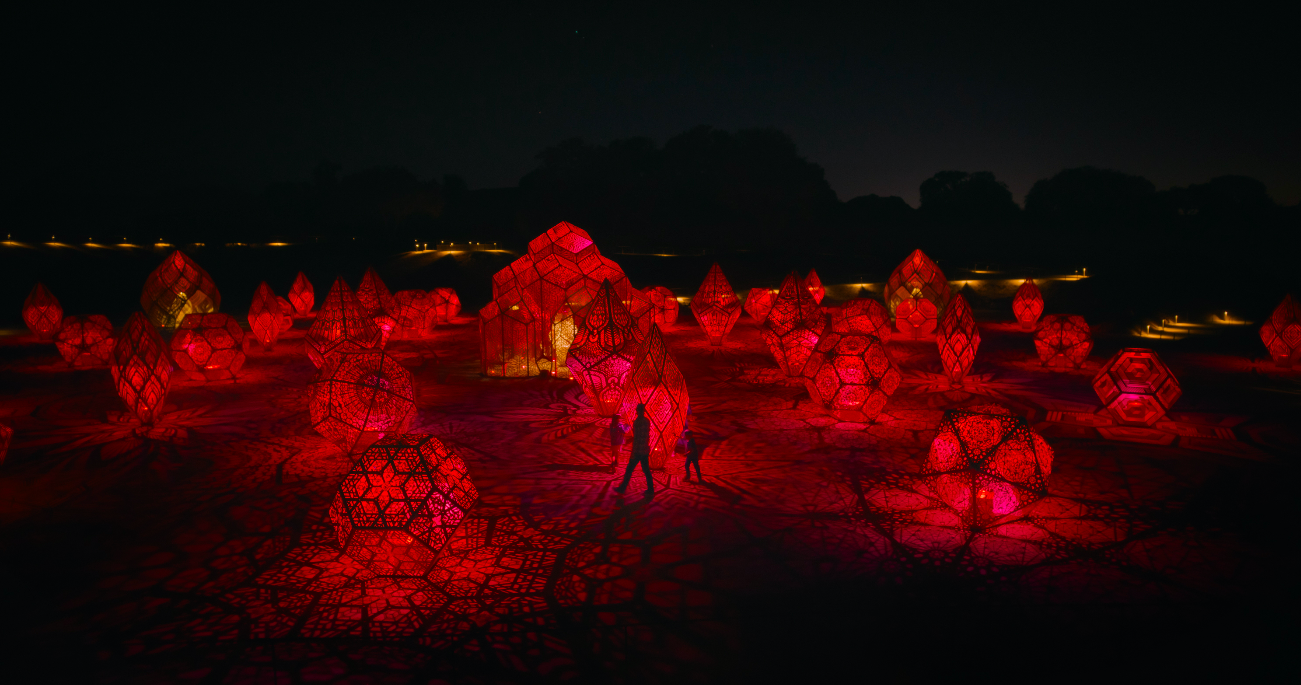 people standing in front of a red light sculpture display at night